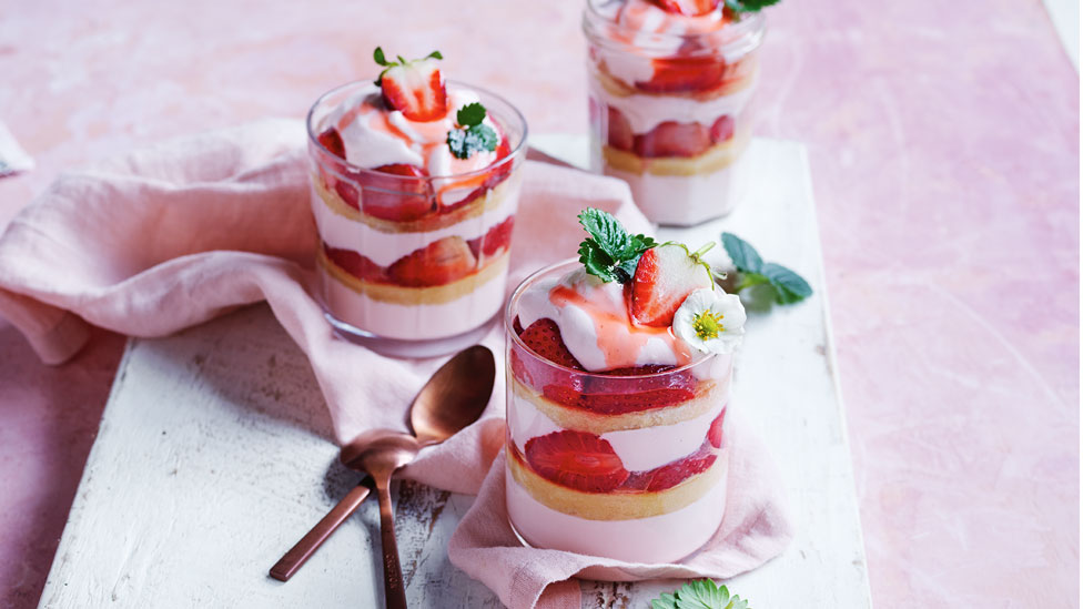 Three Strawberry Shortcake Trifles in glass cups served on a concrete platter with spoons beside the cups