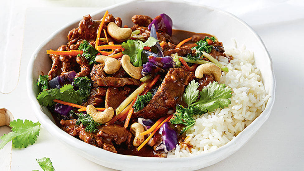 Beef stir-fry served in a bowl with rice and coriander and cashew nuts on top