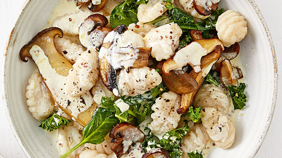 Mushrooms and kale tossed with gnocchi and cream served in a bowl