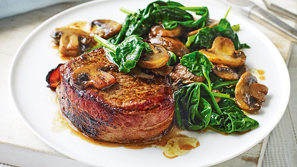 Bacon-wrapped beef served on a plate with garlic mushrooms and spinach