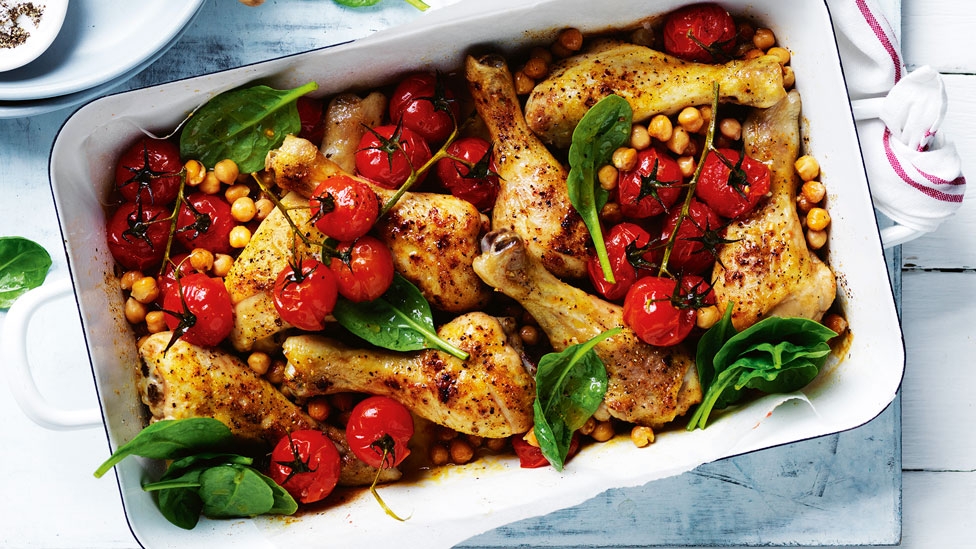 Chicken drumsticks and chickpea tray bake with roasted tomatoes and spinach leaves