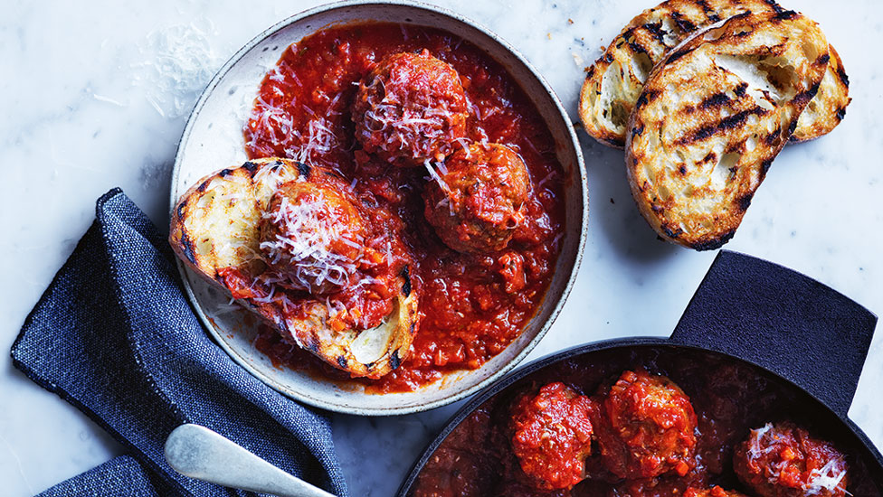 Curtis Stone's Homemade Meatballs served on bread with cheese. Arranged on a marble table with navy towels. Served with chargrilled bread.