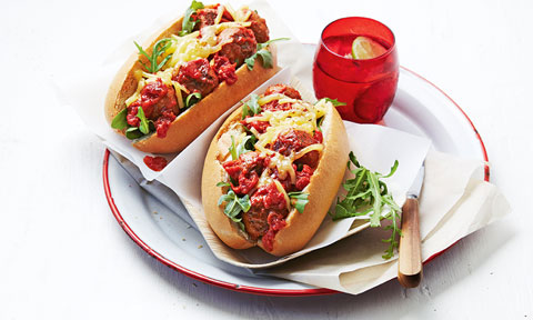 Two meatball subs on a plate with loose rocket leaves