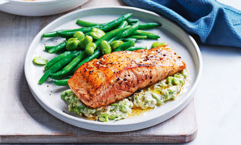 Garlic Salmon served on a plate on top of broad bean hommus with green beans and broad beans on the side