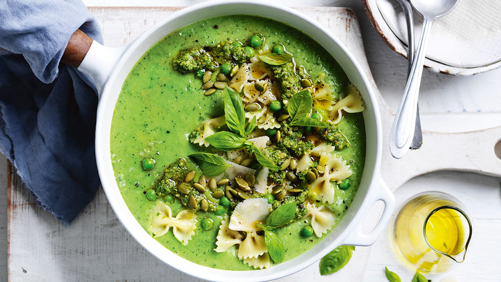 Green Pesto Vegetable Soup in white dish. Olive oil in a glass jub and a white towel.