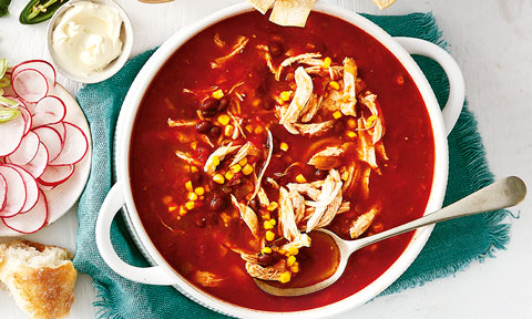 Mexican Chicken Soup in bowl on teal cloth. Served with radish, sour cream and bread
