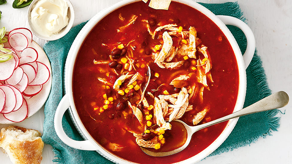 Mexican Chicken Soup in bowl on teal cloth. Served with raddish, sour cream and bread