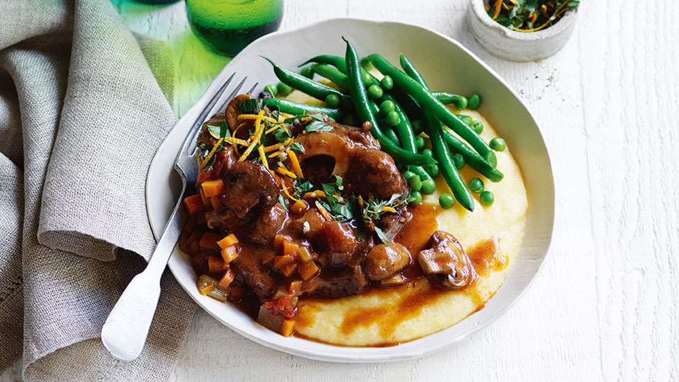 Osso Bucco with Mushroom and Red Wine Sauce on polenta with peas and beans. Next to a grey cloth.