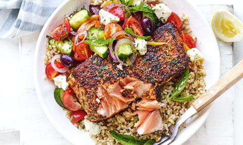Paprika Salmon and Greek Salad Bowl, served with brown rice, garnished with lemon zest.