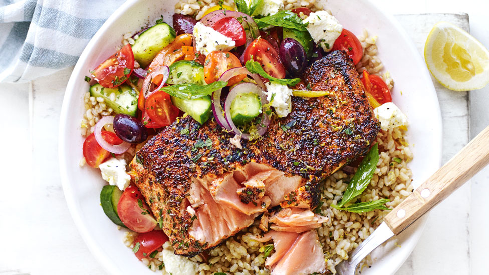 Paprika Salmon and Greek Salad Bowl, served with brown rice, garnished with lemon zest.