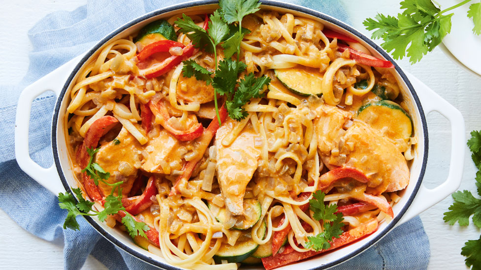 Red Curry Salmon Linguine in white dish with a blue towel and coriander