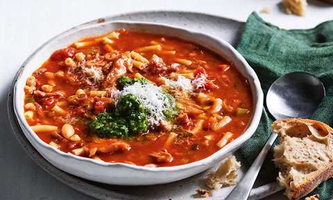 Slow Cooker Ham Hock Minestrone garnished with pesto and cheese, beside bread and green cloth