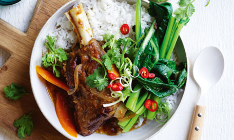 Slow Cooker Mongolian Lamb Shanks on rice, garnished with chilli and spring onion. Placed on a wooden cutting board.
