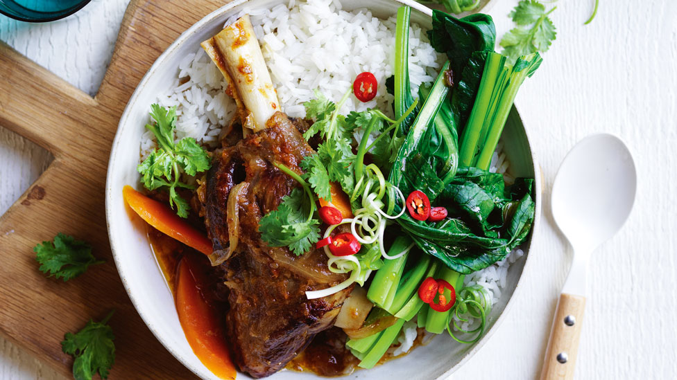 Slow Cooker Mongolian Lamb Shanks on rice, garnished with chilli and spring onion. Placed on a wooden cutting board.