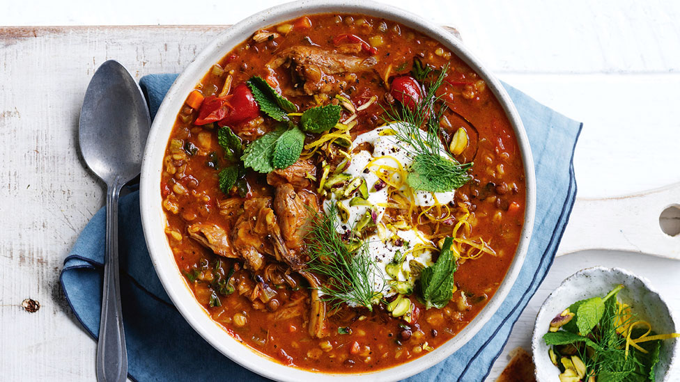 Slow Cooker Moroccan-style Lamb and Lentil Soup garnished with mint, lemon zest and pistachio. With side salad and white cloth.