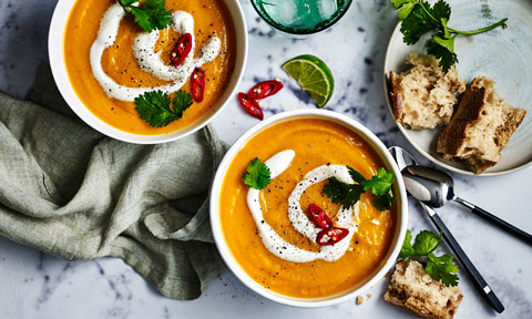 Two bowls of Slow-cooker Thai-style pumpkin soup with yoghurt and parsley. Served with bread and lime.