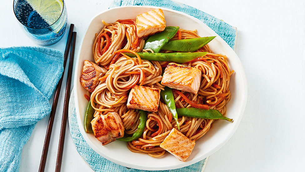 Salmon chunks served in a bowl with noodle stir-fry and snow peas