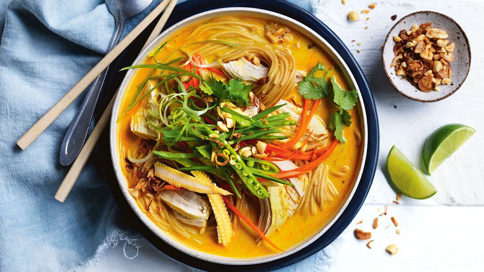 Thai Chicken and Ramen Noodle Soup in bowl, served with lime and peanutes. Placed upon a blue cloth