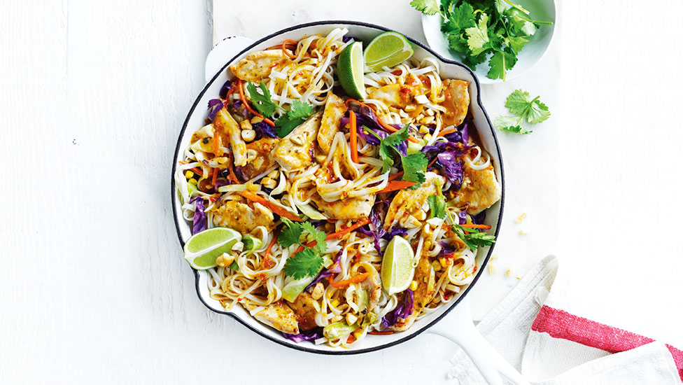 Dish with Thai-style chicken and noodle stir-fry, with lime wedges and a side bowl of coriander sprigs