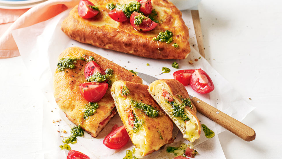 Tomato, Pesto and Mozzarella Calzone on baking paper with knife