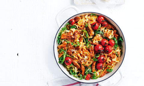 Tomato pesto chicken pasta served in a casserole dish with greens and roasted tomatoes