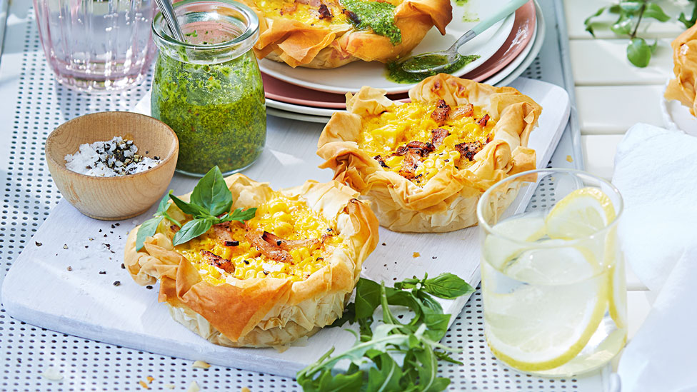 Two bacon and corn quiches with pesto, oil and salad