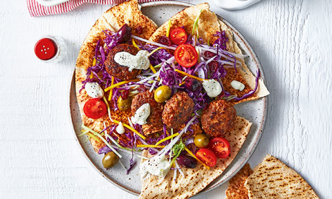 A stack of pita bread with beef meatballs, topped with a mediterran salad