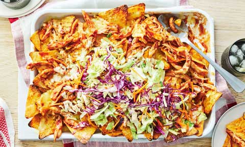 Chicken nachos served in two bowls with avocado, red onion and tomatoes