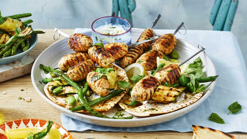A bowl of chicken kofta skewers with green beans and pita bread.