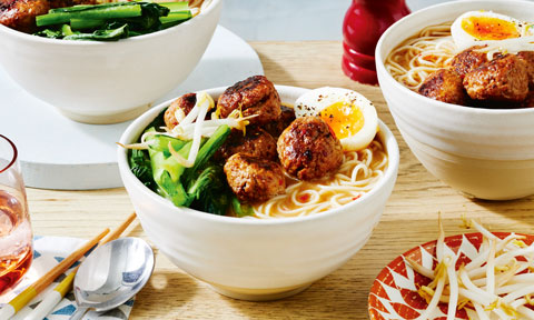 Bowls of pork tantanmen meatballs with jammy eggs, green veggies and noodles in broth.