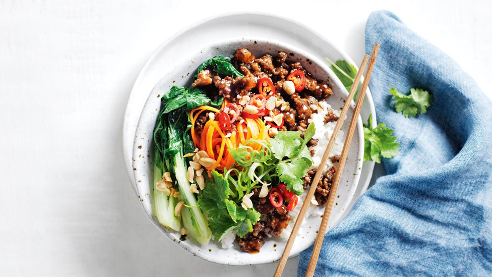 A bowl of mongolian styled beef on rice with veggies