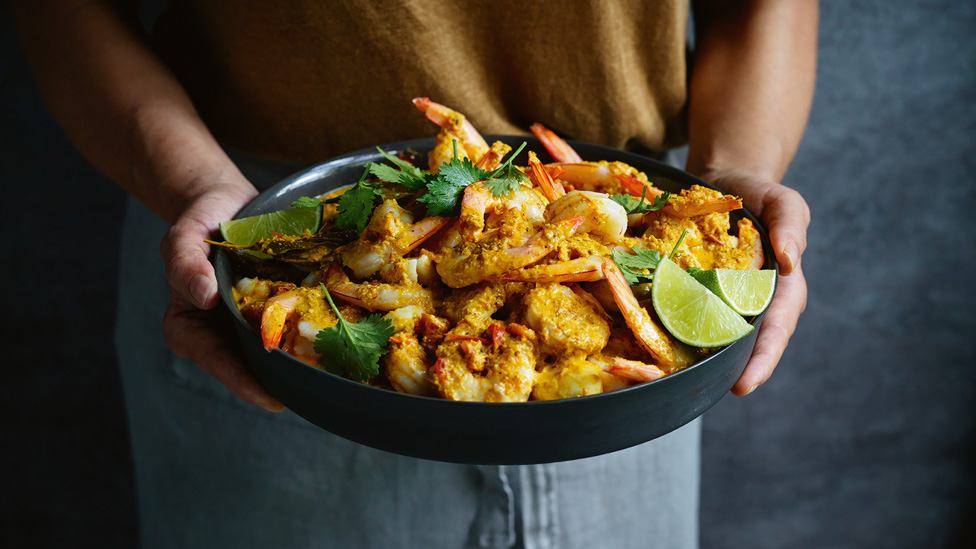 A pair of hands holding a bowl of prawn and scallop curry