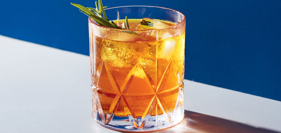 A glass of whisky with a rosemary sprig