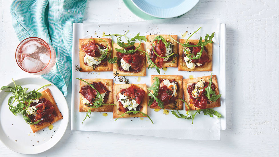 Several prosciutto, cranberry and goat’s cheese mini tarts on a dish, garnished with rocket.