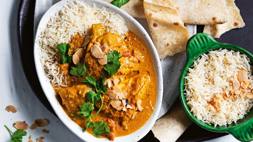 A bowl of slow cooked chicken korma on rice served with naan