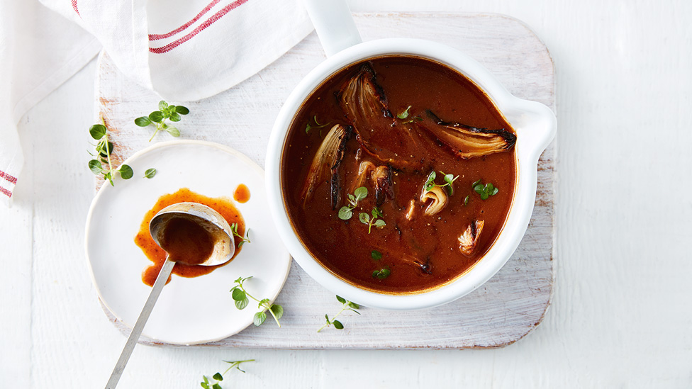 A pot of Vegemite gravy with a ladle and fresh herbs on the side