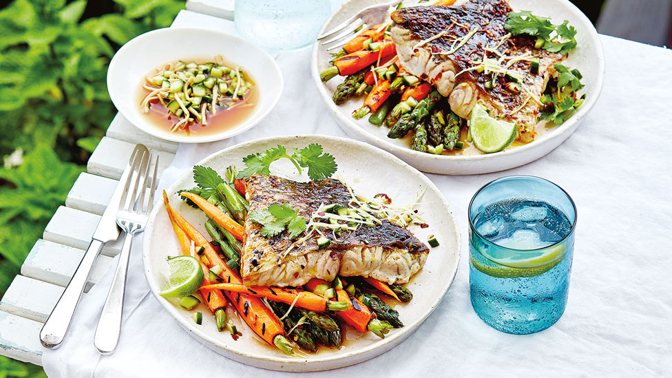 Two bowls of bbq chilli barramundi with carrot and asparagus, served with ginger and cucumber dressing