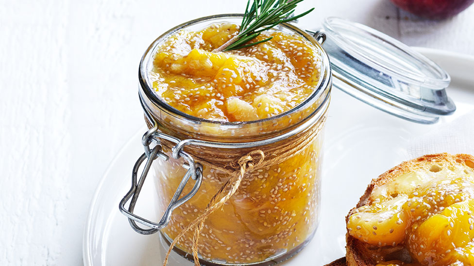 A glass jar of peach and maple chia jam topped with rosemary