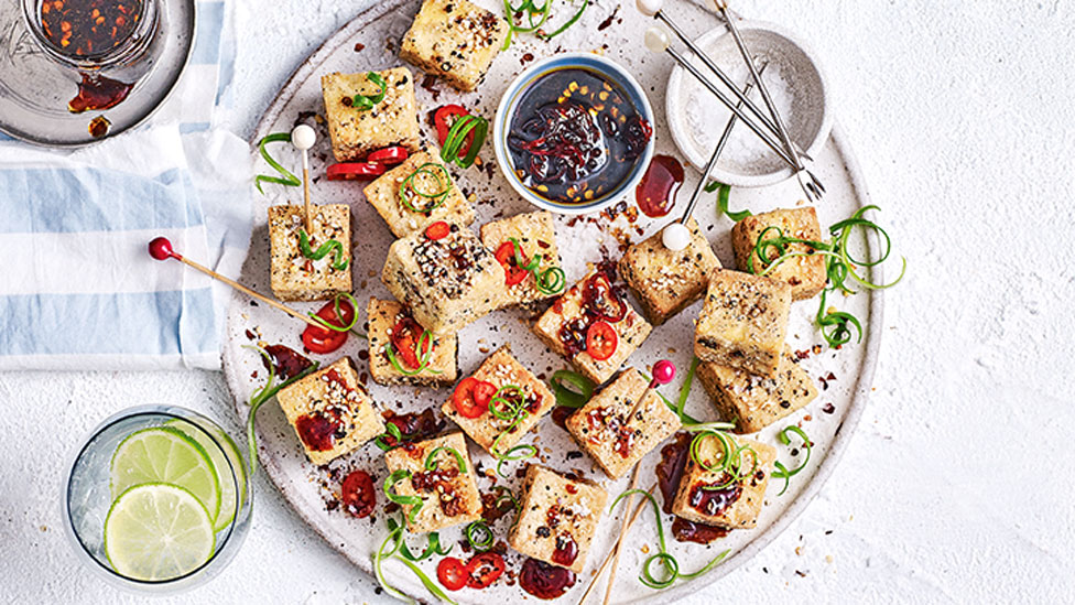 Platter of gluten free salt and pepper tofu squares, dressed in thinly sliced red chilli, spring onion curls and toasted sesame seeds.
