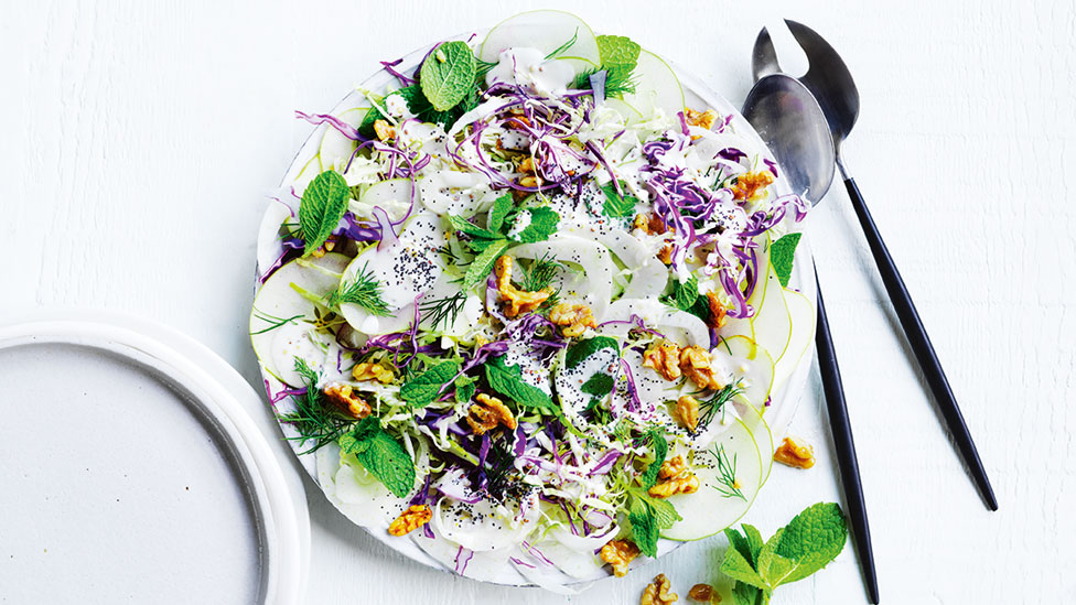 Cabbage, apple and poppy seed salad on a dish with two spoons on the side and a mint leaf garnish.