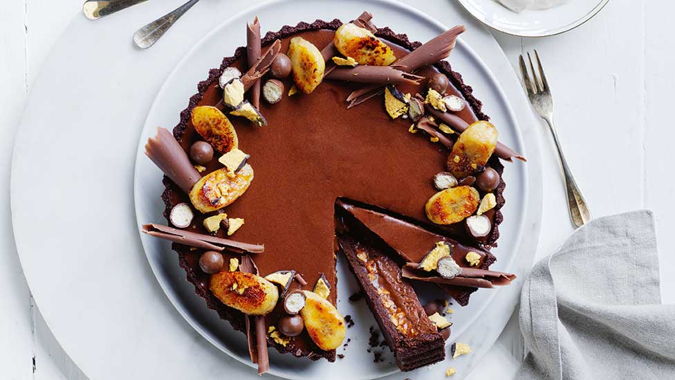 Double choc-caramel peanut tart with chocolate curls and banana slices on top