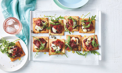 Several prosciutto, cranberry and goat’s cheese mini tarts on a dish, garnished with rocket.