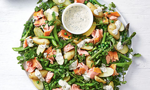 A hot smoked salmon and potato salad served with dressing in a bowl