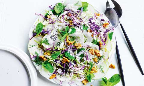 Cabbage, apple and poppy seed salad on a dish with two spoons on the side and a mint leaf garnish.