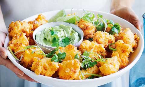 A bowl of mexican style corn fritters served with smashed avocado