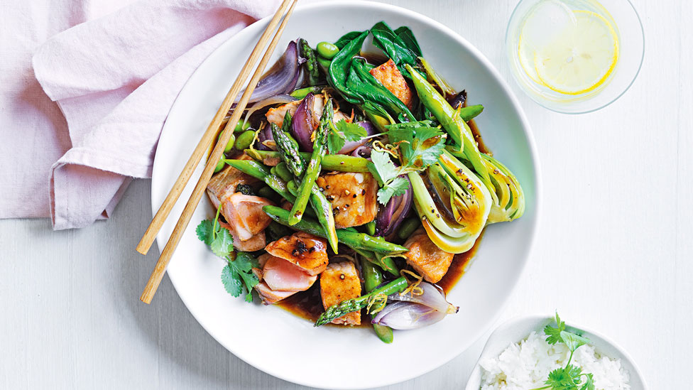 Asparagus, bok choy and salmon stir-fry in a bowl with chopsticks on the side
