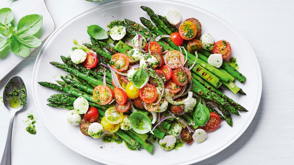 BBQ asparagus served on a big plate with cherry tomatoes and cheese on top