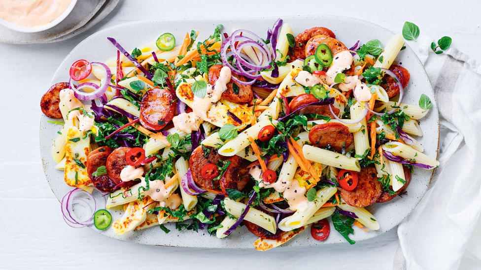 A serving platter of chorizo and pasta salad with red onion and parsley on top