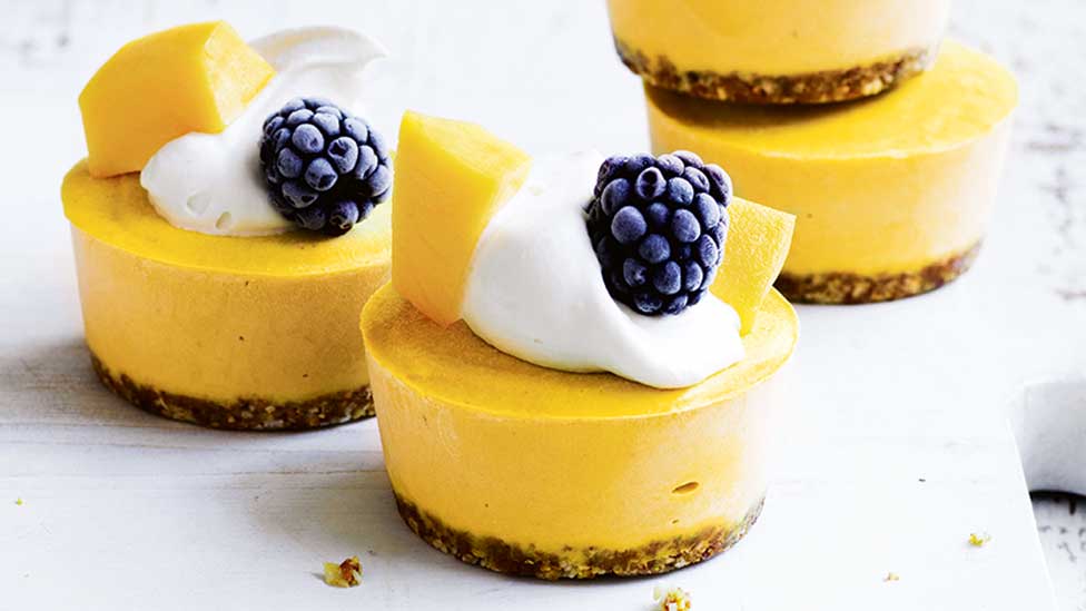 Three mini raw mango cheesecakes with blackberries on top