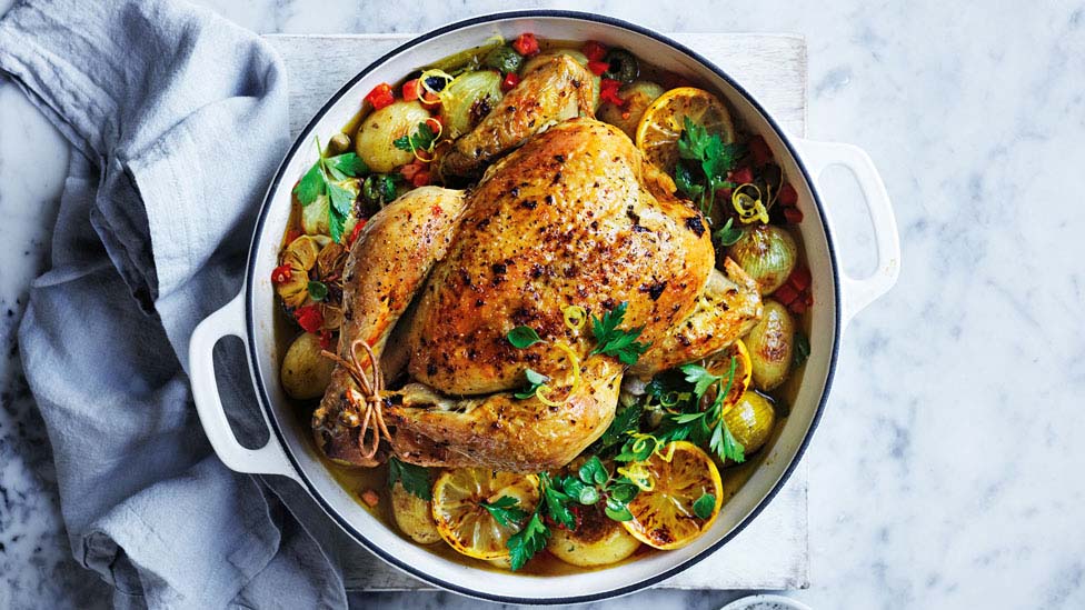 A roast chicken in a baking pot with lemon and parsley